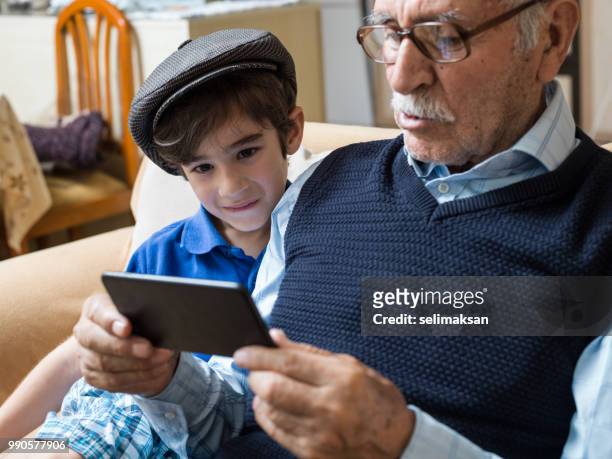 ritratto di bisnonno e nipote guardando il cellulare i̇n soggiorno - selimaksan foto e immagini stock