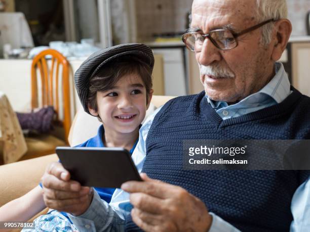 曽祖父と孫の携帯電話 i̇n リビング ルームを見ての肖像画 - 曾孫息子 ストックフォトと画像