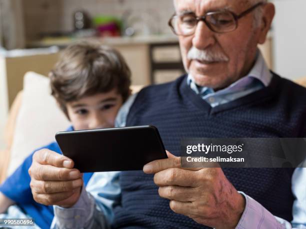 portrait of great grandfather and grandson looking at mobile phone i̇n living room - great grandson stock pictures, royalty-free photos & images