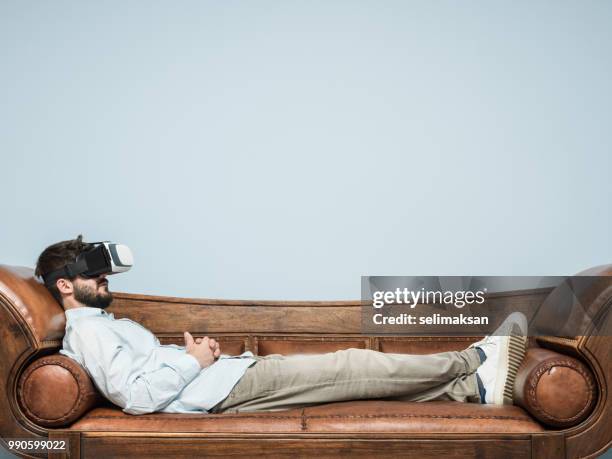 adult man with vr headset lying down on psychiatrist couch - psychiatrists couch stock pictures, royalty-free photos & images