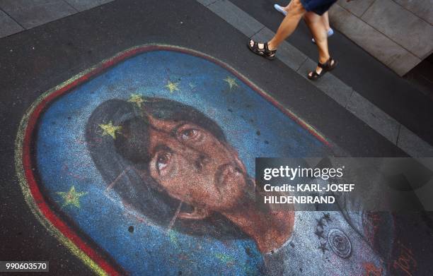 Pedestrians walk past a pavement painting that depicts the head coach of Germany's national football team Joachim Loew on July 3, 2018 in Wuerzburg,...