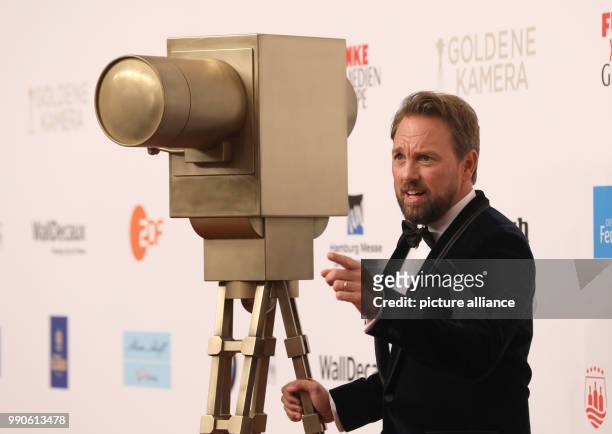 February 2018, Germany, Hamburg, Golden Camera Awards Ceremony: Moderator Steven Gaetjen poses next to a fake camera. Photo: Georg Wendt/dpa