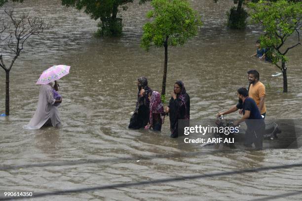 Pakistani residents wade through a flooded street during heavy rain in Lahore on July 3, 2018.