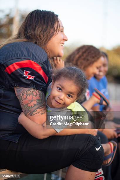 Jeanette Jimenez of the LA Warriors women's tackle football team sits on the sideline with her son during their game against the Portland Fighting...