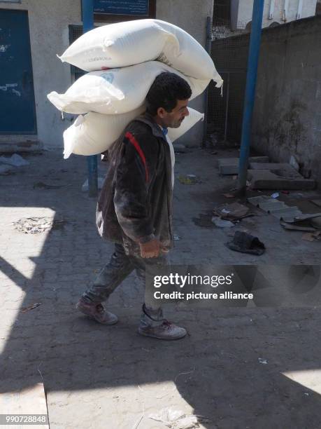 Young man carries flour sacks to an aliment distribution centre of UNRWA in Gaza, Palestinian Territories, 13 February 2018. His clothes are covered...