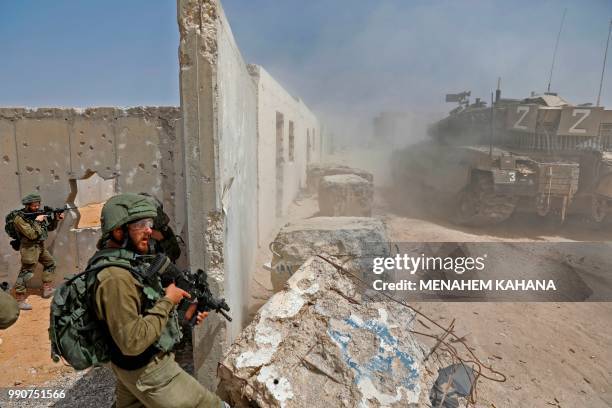 Israeli soldiers from the Kfir brigade's Shimshon battalion take cover behind a wall as a Merkava battle tank drives past during a military exercise...