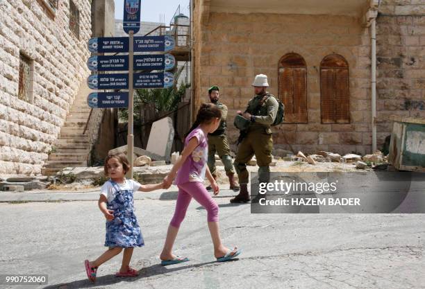 Palestinian girls pass by Israeli soldiers during a visit by former Israeli soldier Elor Azaria to friends in the settlement of Tal Rumeida in the...