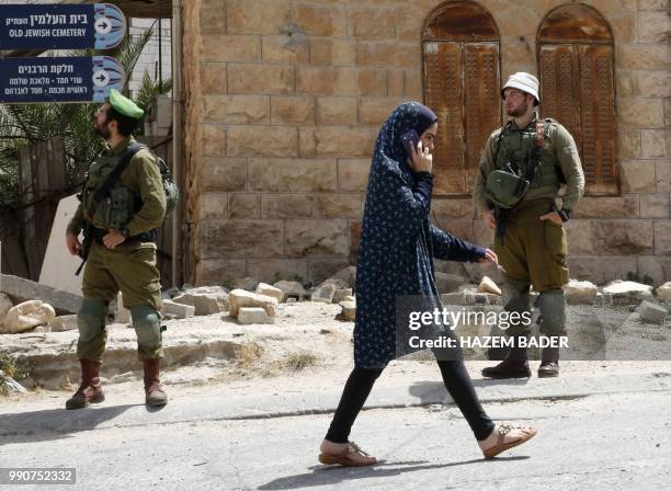 Palestinian girl talks on her mobile phone passes by Israeli soldiers during a visit by former Israeli soldier Elor Azaria to friends in the...