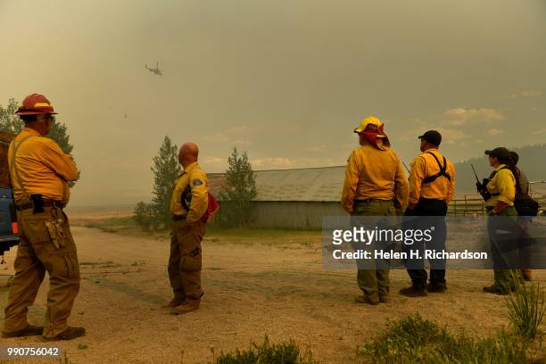 Firefighters wait outside a home to protect it from the Weston Pass Fire as a helicopter flies by to make a water drop on July 2, 2018 near FairPlay,...