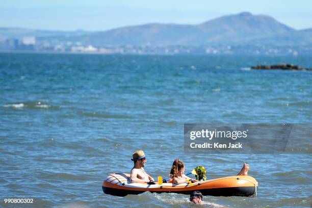 Two people relax in an inflatable dinghy off Silver Sands beach at the start of the Scottish school holidays as the heatwave continues, with...