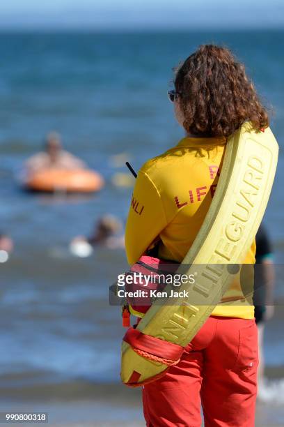 An RNLI lifeguard keeps watch looks towards an inflatable dinghy as people enjoy the sun on Silver Sands beach at the start of the Scottish school...