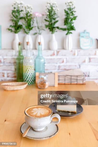 a white cup of hot latte art coffee and coconut cake on the wooden table with the flower in white vase, nature background in coffee shop. - coffee white background stock pictures, royalty-free photos & images