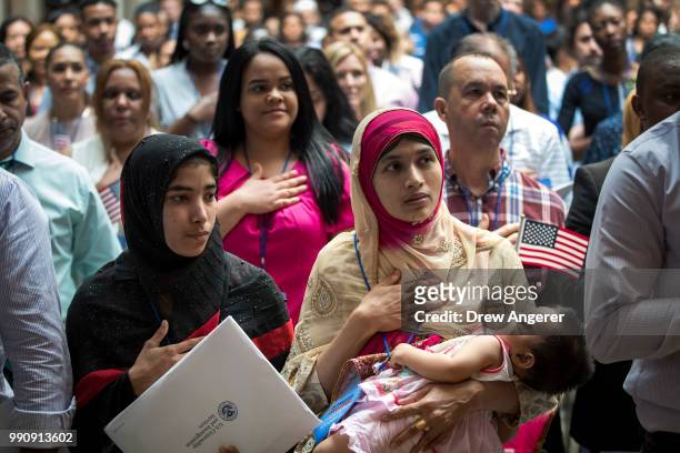 Mosammat Rasheda Akter, originally from Bangladesh, holds her 7 month-old daughter Fahmida as she recites the Pledge of Allegiance after officially...
