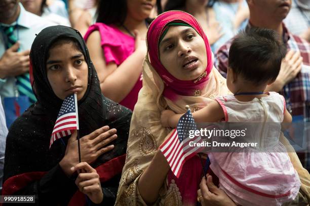 New U.S. Citizen Mosammat Rasheda Akter, orginally Bangladesh, holds her 7 month-old daughter Fahmida as she sings the U.S. National Anthem during...