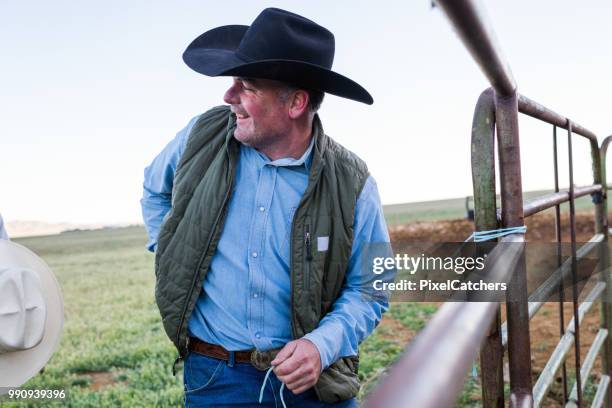 candid portrait rancher smiling to others as he helps build fence - rancher stock pictures, royalty-free photos & images