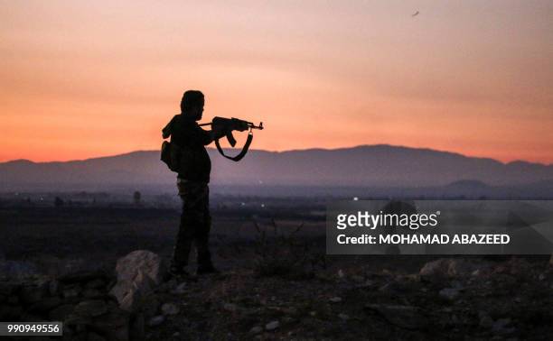Syrian rebel fighter aims his Kalashnikov assault rifle as he stands near the frontline against government forces west of the embattled southern city...