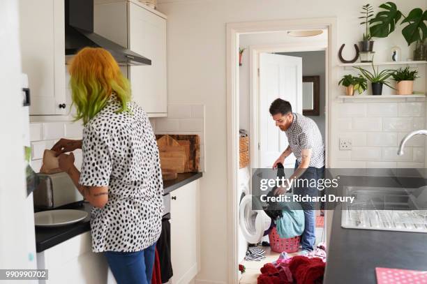 young hipster couple doing laundry and making toast in their kitchen - role reversal stock-fotos und bilder