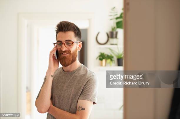 young hipster man using a smart phone in his kitchen - richard drury stock pictures, royalty-free photos & images