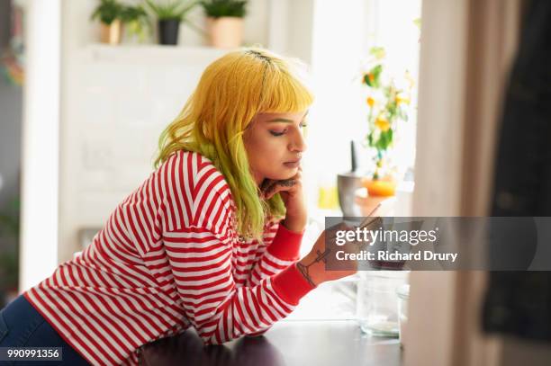 young hipster woman using a smart phone in her kitchen - richard drury stock pictures, royalty-free photos & images