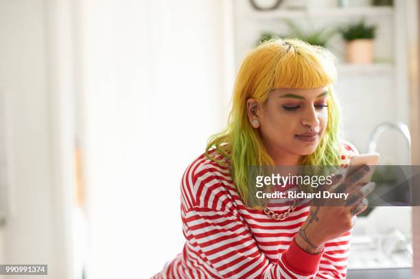 young hipster woman using a smart phone in her kitchen - richard drury stock pictures, royalty-free photos & images