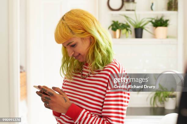 young hipster woman using a smart phone in her kitchen - richard drury stock pictures, royalty-free photos & images