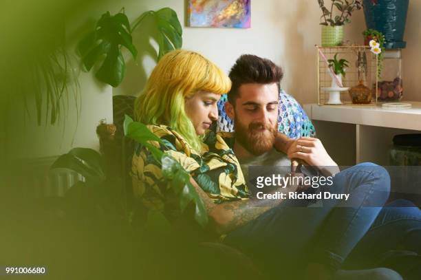 young married hipster couple sitting together in their living room - living room young couple stock-fotos und bilder