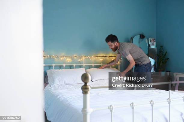 young hipster man making his bed - richard drury stock pictures, royalty-free photos & images