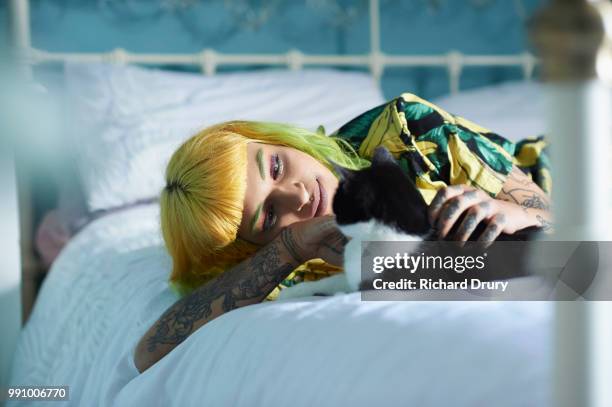 hipster woman lying on her bed stroking her pet cat - richard drury stock pictures, royalty-free photos & images