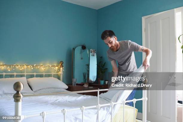 young hipster man making his bed - rolwisseling stockfoto's en -beelden