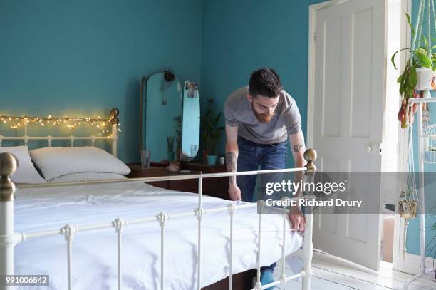 young hipster man making his bed - richard drury stock pictures, royalty-free photos & images