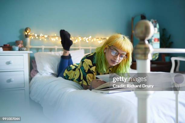 young hipster woman lying on her bed reading a book - richard drury stock pictures, royalty-free photos & images