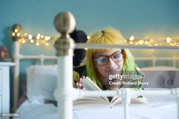 young woman lying on her bed reading a book - richard drury stock pictures, royalty-free photos & images