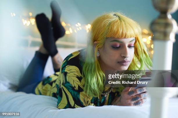young hipster woman lying on her bed using her smart phone - richard drury stock pictures, royalty-free photos & images