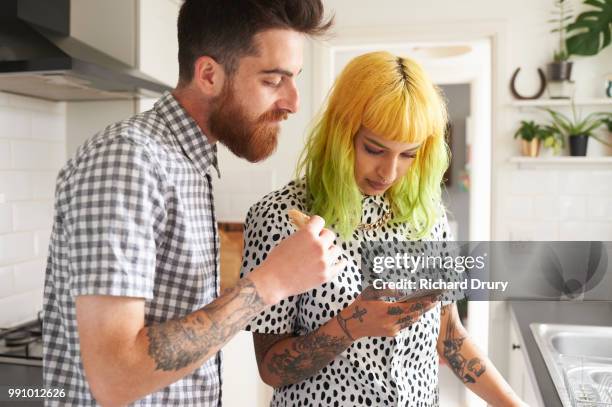 young hipster couple looking at a smart phone in their kitchen - hipster in a kitchen stock-fotos und bilder
