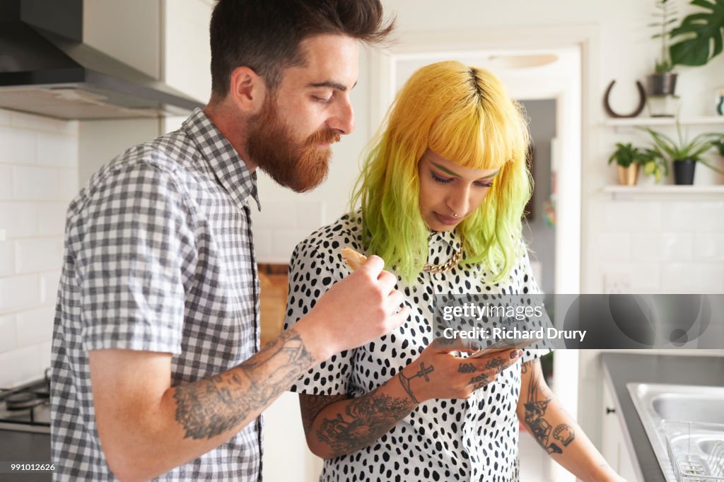 Young hipster couple looking at a smart phone in their kitchen