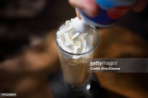 whipped cream being sprayed into a tall glass of iced coffee - aufschäumen stock-fotos und bilder
