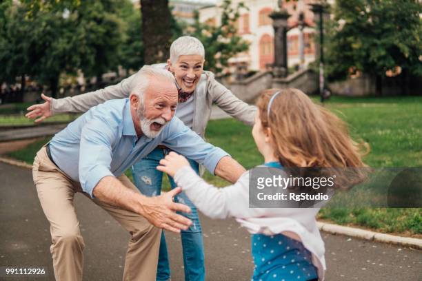 granddaughter running into arms of her grandparents - embracing stock pictures, royalty-free photos & images