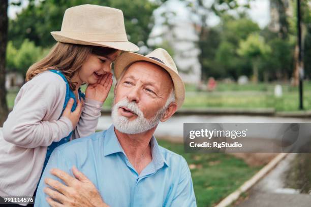 old man listening his granddaughter whispering to him - granddaughter stock pictures, royalty-free photos & images