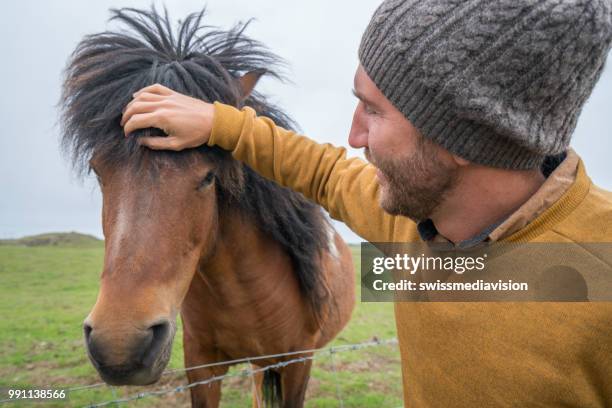 junger mann petting islandpferd in wiese, menschen reisen reise-tier-konzept - animal mane stock-fotos und bilder