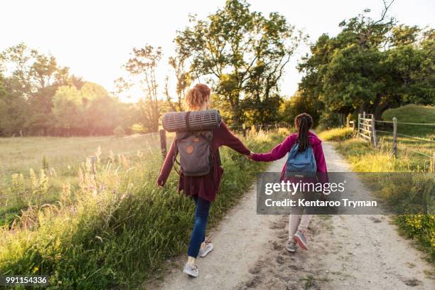 rear view of mother and daughter holding hands while hiking on dirt road in forest - backpacker road stockfoto's en -beelden