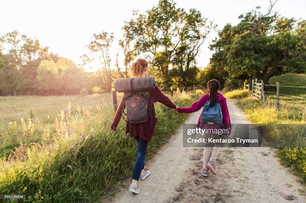 Rear view of mother and daughter holding hands while hiking on dirt road in forest