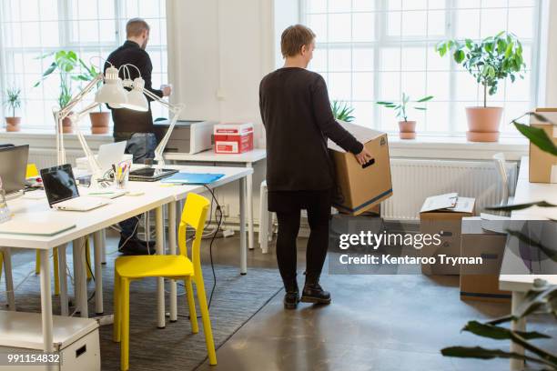 rear view of businesswoman carrying cardboard box by desk in creative office - moving office stock-fotos und bilder