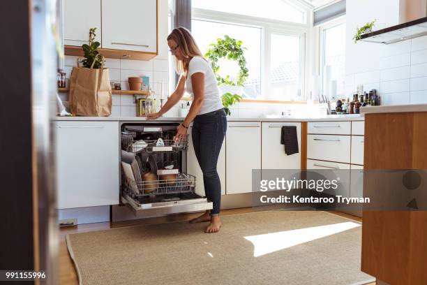 full length of woman using dishwasher while standing in kitchen - dishwasher stock pictures, royalty-free photos & images