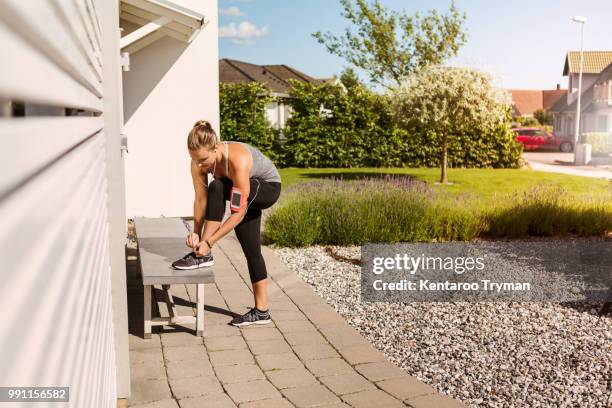 full length of woman tying shoes on bench in backyard during sunny day - attacher photos et images de collection