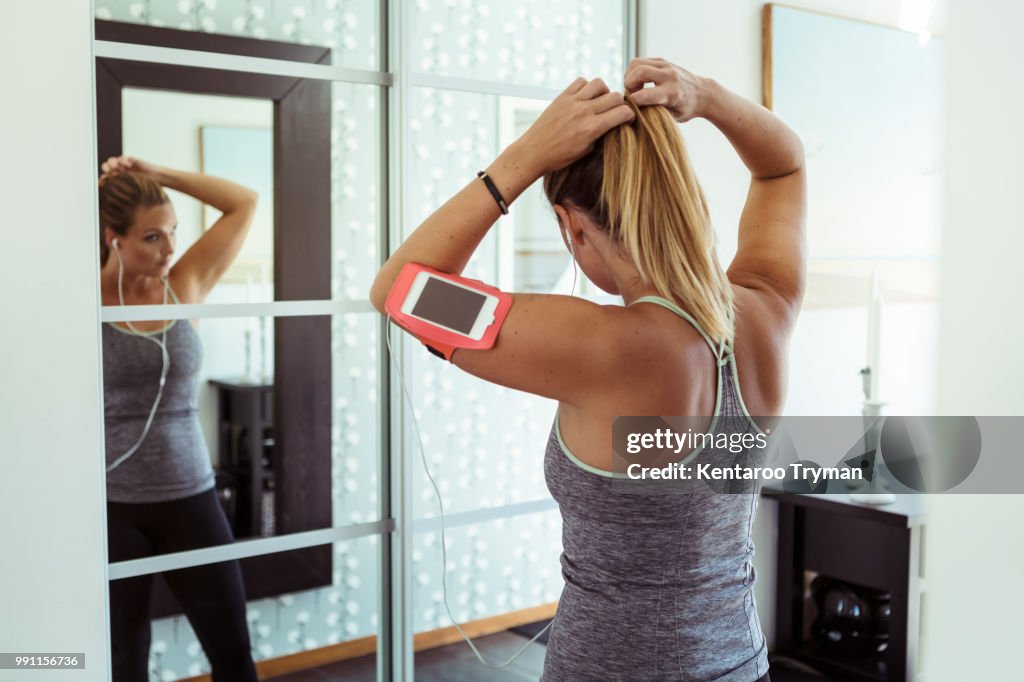 Woman in sport clothing tying ponytail while looking in mirror at home