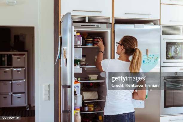 rear view of woman looking into refrigerator while standing in kitchen - fridge door stock-fotos und bilder