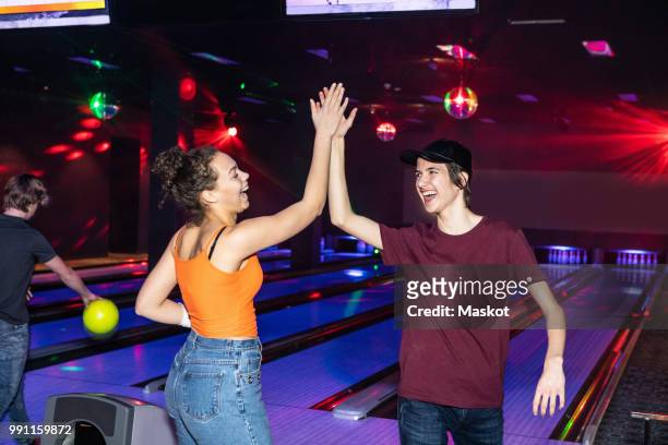 cheerful friends giving high-five on parquet floor at bowling alley - bowling stock-fotos und bilder