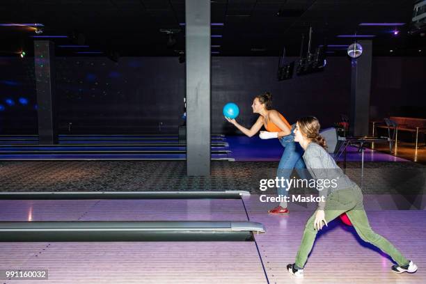 full length of teenage girls throwing balls on parquet floor at bowling alley - bowling alley stock pictures, royalty-free photos & images