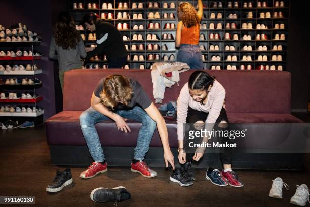teenage boy helping friend wearing shoes while sitting on sofa at bowling alley - tool rack ストックフォトと画像