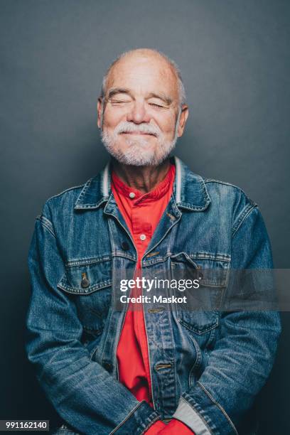 smiling senior man with eyes closed standing against gray background - weiße jacke stock-fotos und bilder